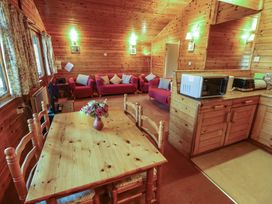 A wooden dining table with flowers a microwave toaster and kettle on a wooden counter and red couches with cushions in a wooden room at Kestrel in Withern near Alford