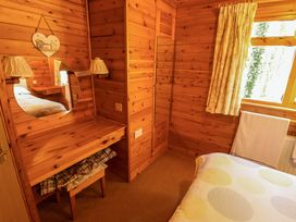 A wooden bedroom with a dressing table a round mirror a bed with patterned bedding and a window with curtains at Kestrel in Withern near Alford
