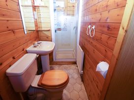 A small bathroom with wooden walls a toilet with wooden seat a pedestal sink and a shower cubicle at Kestrel in Withern near Alford