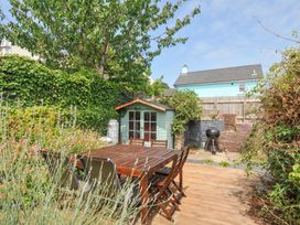 A garden with a wooden table, chairs, shed, and grill at 12 Alpha Place Appledore