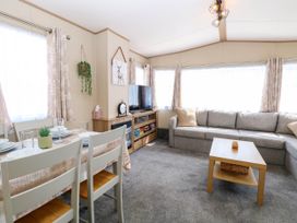 A living room with a gray sofa a wooden coffee table a dining table with chairs and a television on a cabinet at Oakley Retreat in Fritton near Belton