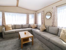 A living room with a gray corner sofa beige cushions a wooden coffee table and windows with curtains at Oakley Retreat in Fritton near Belton