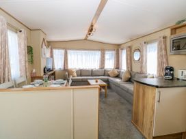 A living room with a large gray sectional sofa with pillows a wooden coffee table a dining area with table set for four windows with curtains and a kitchen counter with appliances at Oakley Retreat in Fritton near Belton