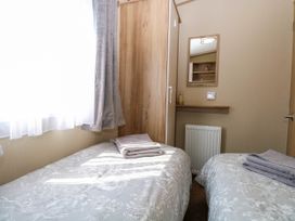A small bedroom with two single beds each with folded towels a wooden wardrobe a mirror above a small shelf and a radiator at Oakley Retreat in Fritton near Belton