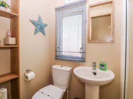 A bathroom with a toilet and a sink under a window with blinds and a wooden framed mirror on the wall at Oakley Retreat in Fritton near Belton