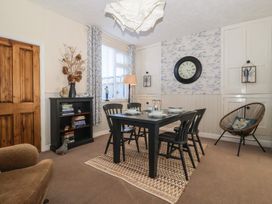 A dining room with a black table and chairs a bookshelf with books a floor lamp and a wall clock at 48 Waxholme Road in Withernsea