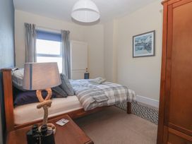A bedroom with a wooden bed with striped bedding a wooden wardrobe bedside table with a lamp and binoculars a window with curtains and a framed picture on the wall at 48 Waxholme Road in Withernsea