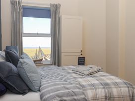 A bedroom with a bed with pillows and a blanket near a window with curtains and a model sailboat on the windowsill at 48 Waxholme Road in Withernsea