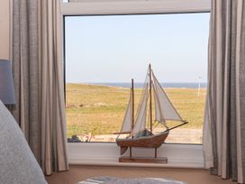 A window with a model sailboat on the sill and curtains on both sides overlooking a grassy field and sea at 48 Waxholme Road in Withernsea
