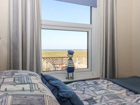 A bedroom with a bed near a window with curtains and a figurine on the windowsill at 48 Waxholme Road in Withernsea