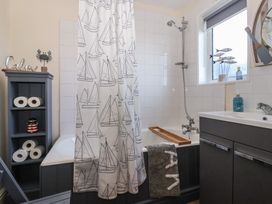 A bathroom with a bathtub and shower curtain with boat designs a gray shelf with toilet paper rolls and a lighthouse decoration a window with fish decorations a sink with soap dispenser and a towel on the bathtub at 48 Waxholme Road in Withernsea