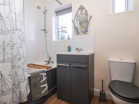 A bathroom with a bathtub and shower, a sink with cabinet, a toilet, and a mirror shaped like a boat at 48 Waxholme Road Withernsea