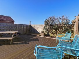 An outdoor wooden deck with blue metal chairs and a wooden picnic table surrounded by a wooden fence at 48 Waxholme Road in Withernsea