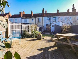 A backyard with wooden deck seating blue chairs a picnic table a garden shed and terraced houses at 48 Waxholme Road in Withernsea