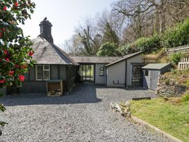 The exterior of a stone cottage with a slate roof and wood storage next to a gravel driveway and garden at Bwthyn y Coediwr The Woodcutters Cottage in Tan Y Bwlch Maentwrog