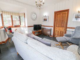 A living room with a gray sofa a gray armchair a television and wooden door at Bwthyn y Coediwr The Woodcutters Cottage in Tan Y Bwlch Maentwrog