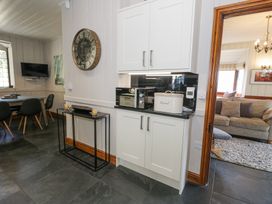 A kitchen with white cabinets a microwave and breadbin next to a dining area and living room at Bwthyn y Coediwr The Woodcutters Cottage in Tan Y Bwlch Maentwrog