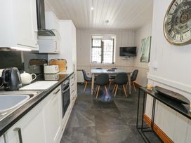 A kitchen with a dining table and chairs and a wall clock at Bwthyn y Coediwr The Woodcutters Cottage in Tan Y Bwlch Maentwrog