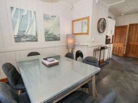 A dining area with a glass table and six chairs with paintings and a mirror on the wall at Bwthyn y Coediwr The Woodcutters Cottage in Tan Y Bwlch Maentwrog