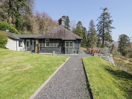 A cottage with slate roof and gravel pathway surrounded by grass and trees at Bwthyn y Coediwr in Tan Y Bwlch Maentwrog
