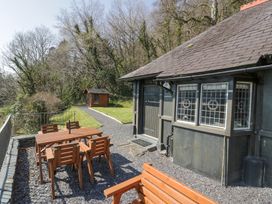 An outdoor area with a wooden table and chairs next to a building with leaded windows and a gravel path leading to a shed at Bwthyn y Coediwr The Woodcutters Cottage in Tan Y Bwlch Maentwrog