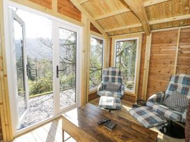 A wooden room with two plaid armchairs a wooden table and large glass doors at Bwthyn y Coediwr The Woodcutters Cottage in Tan Y Bwlch Maentwrog