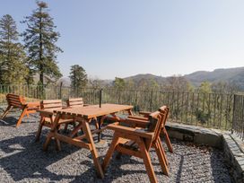 An outdoor seating area with wooden table and chairs on a gravel terrace overlooking trees and hills at Bwthyn y Coediwr The Woodcutters Cottage in Tan Y Bwlch Maentwrog