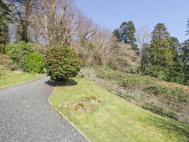 A gravel driveway with a bush in the middle next to a grassy area and trees at Bwthyn y Coediwr The Woodcutters Cottage in Tan Y Bwlch Maentwrog