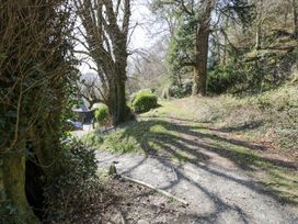 A dirt path with trees and bushes alongside and a building partially visible in the background at Bwthyn y Coediwr The Woodcutters Cottage in Tan Y Bwlch Maentwrog