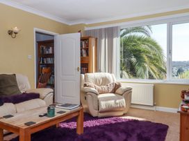 A living room with a beige armchair a wooden coffee table bookshelves and a large window showing palm trees at House of Emma in Paignton