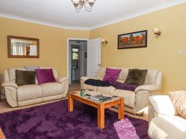 A living room with two beige sofas with cushions a wooden coffee table with books and a candle a large purple rug a mirror on one wall and a painting of elephants on another wall at House of Emma in Paignton