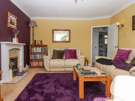 A living room with beige sofas and purple cushions a wooden coffee table with books a purple rug a bookshelf and a fireplace at House of Emma in Paignton