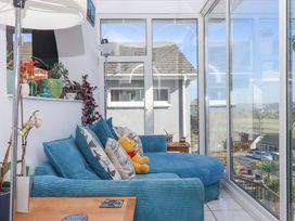 A sunroom with a blue chaise sofa with cushions and a teddy bear near glass doors and windows overlooking a neighborhood at House of Emma in Paignton