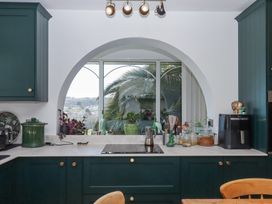A kitchen with green cabinets white countertop and an arch window overlooking trees and houses at House of Emma in Paignton