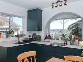 A kitchen with dark green cabinets a brass faucet a black sink and kitchen utensils near arched windows at House of Emma in Paignton