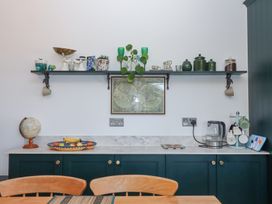A kitchen counter with a globe fruit bowl and kettle beneath a shelf holding plants cups and containers at House of Emma Paignton