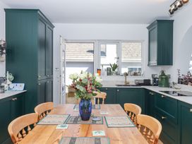 A kitchen with dark green cabinets a wooden table with chairs and a blue vase with flowers at House of Emma in Paignton