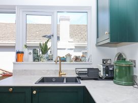 A kitchen sink with gold faucet green cabinets and items on the countertop and windowsill at House of Emma in Paignton