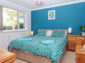 A bedroom with a double bed with patterned bedding a blue accent wall wooden bedside tables and a window at House of Emma in Paignton