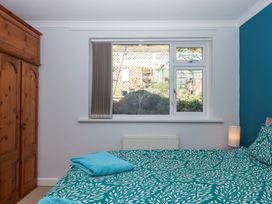 A bedroom with a wooden wardrobe a bed with green patterned bedding and a window showing a garden at House of Emma in Paignton