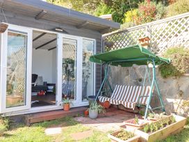 A garden area with a striped swing seat next to a small building with glass doors at House of Emma in Paignton