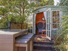 A garden seating area with a table and stools next to a wooden summerhouse with open doors at House of Emma in Paignton