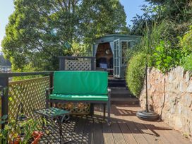 A wooden deck with a green cushioned bench and a glass table next to a stone wall at House of Emma in Paignton