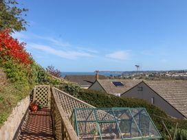 A garden pathway with a wooden trellis fence and greenhouse overlooking rooftops and the sea at House of Emma in Paignton