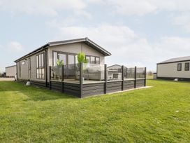 A modern single story house with a glass fenced deck and outdoor furniture on a grassy lawn at Summerdown in Brean