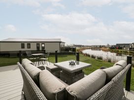 A deck with wicker sofas and a table overlooking a pond and multiple lodges at Summerdown in Brean