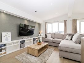 A living room with a large sectional sofa wooden coffee table wall-mounted television and shelves at Summerdown Brean