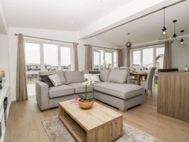 A living room with a gray sectional sofa a wooden coffee table with a plant and dining area with chairs and pendant lights at Summerdown in Brean