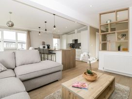 An open-plan living room and kitchen with a beige sofa wooden coffee table with a plant and magazine bar stools at a kitchen island and shelving with plants at Summerdown in Brean