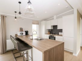A kitchen with a wooden countertop, three bar stools, white cabinets, a built-in oven, and pendant lights at Summerdown Brean